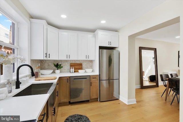 kitchen featuring stainless steel appliances, tasteful backsplash, light countertops, light wood-type flooring, and white cabinets
