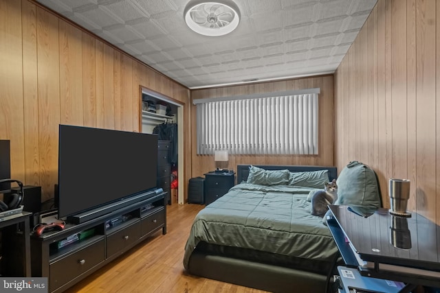 bedroom featuring wooden walls, light wood-style floors, an ornate ceiling, and a closet