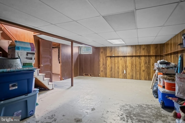 basement featuring wooden walls, stairway, and a paneled ceiling