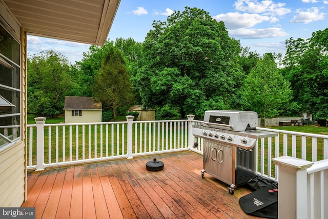 deck with a lawn, an outdoor structure, a grill, and view of wooded area