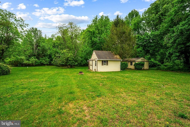 view of green lawn with a shed, an outbuilding, and a forest view