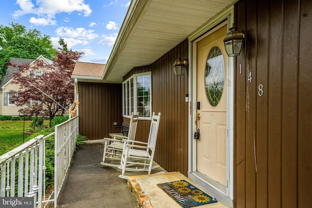entrance to property with covered porch and a shingled roof