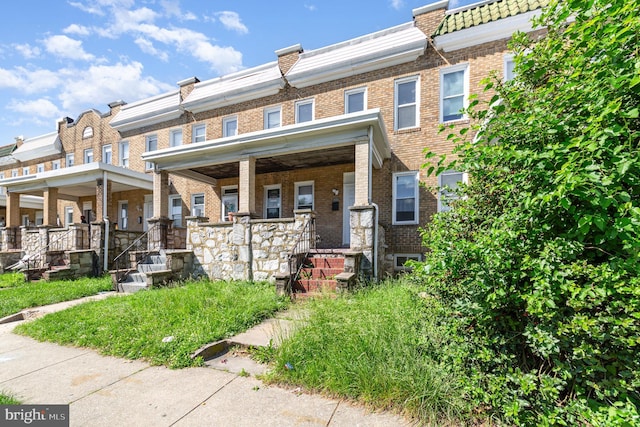 view of property featuring brick siding, covered porch, and mansard roof
