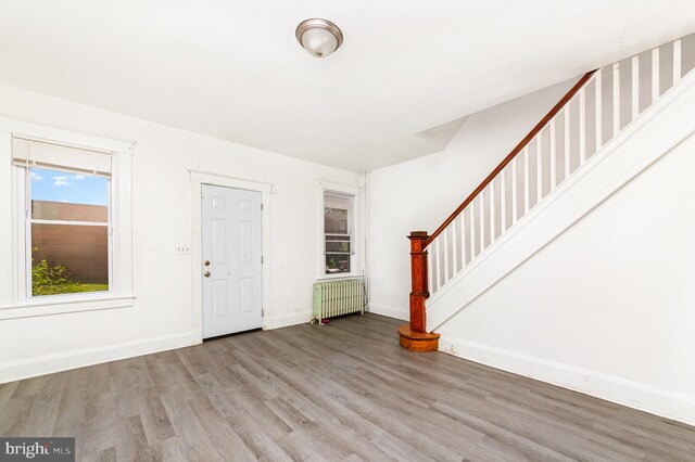 foyer entrance with radiator heating unit, wood finished floors, stairs, and baseboards