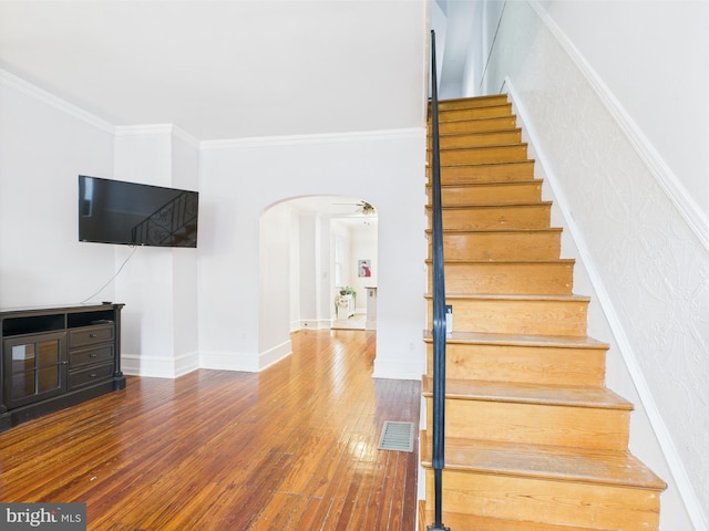 stairs with arched walkways, wood-type flooring, ornamental molding, and baseboards