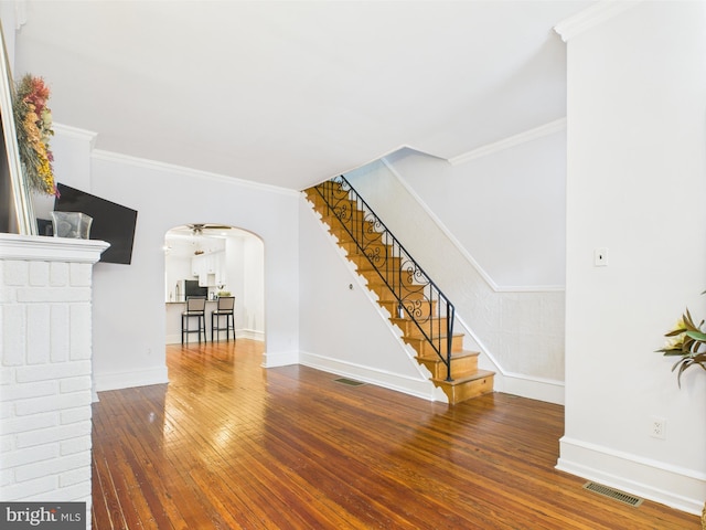 unfurnished living room featuring wood-type flooring, arched walkways, baseboards, stairway, and crown molding