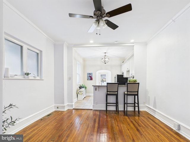 kitchen with a breakfast bar, wood-type flooring, white cabinetry, a peninsula, and crown molding