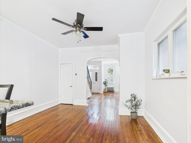 spare room featuring arched walkways, hardwood / wood-style floors, a ceiling fan, stairway, and baseboards