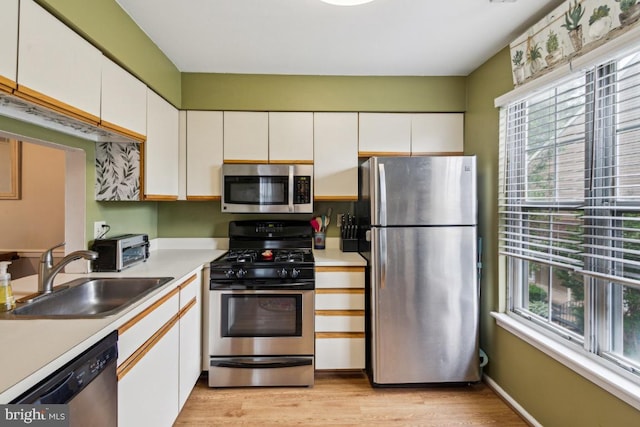 kitchen featuring stainless steel appliances, a sink, light countertops, and white cabinetry