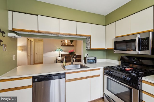 kitchen featuring appliances with stainless steel finishes, a sink, light countertops, and white cabinetry