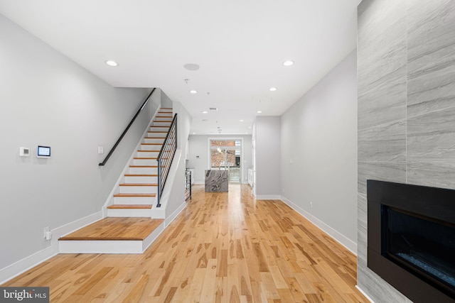 foyer featuring stairs, light wood-type flooring, a tile fireplace, recessed lighting, and baseboards