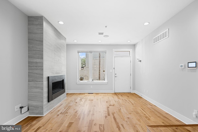 unfurnished living room featuring a tiled fireplace, light wood-type flooring, recessed lighting, and baseboards