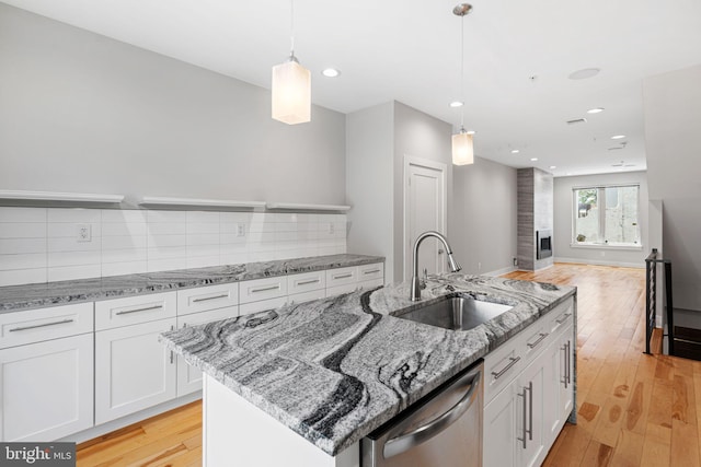 kitchen with a sink, stainless steel dishwasher, white cabinetry, light wood-style flooring, and backsplash