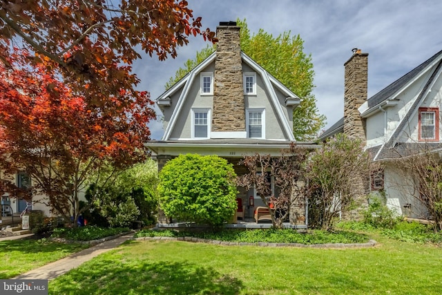 back of house with covered porch, a yard, stucco siding, a chimney, and a gambrel roof