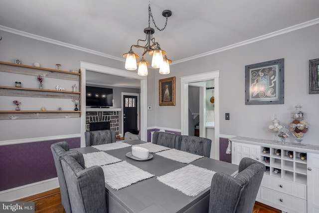 dining space featuring a chandelier, crown molding, baseboards, a fireplace, and dark wood-type flooring
