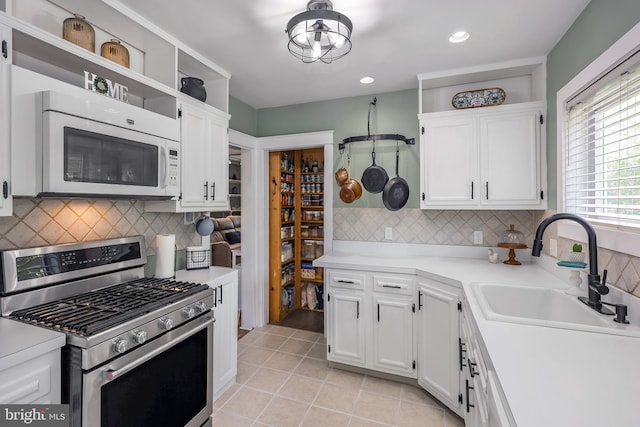 kitchen with stainless steel gas range oven, white microwave, a sink, white cabinetry, and recessed lighting