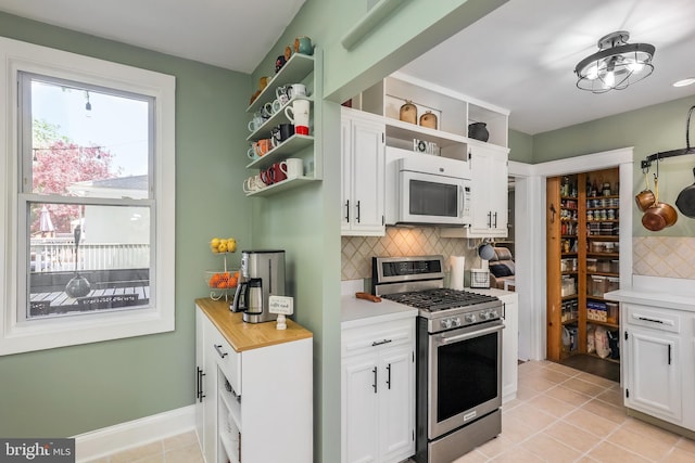 kitchen with stainless steel gas range oven, open shelves, white microwave, light countertops, and white cabinets