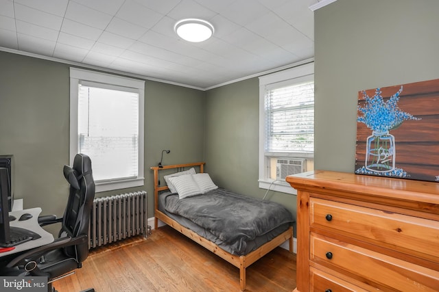 bedroom with radiator heating unit, wood finished floors, ornamental molding, cooling unit, and an office area