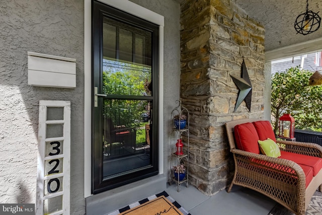 view of exterior entry featuring stucco siding, stone siding, and covered porch