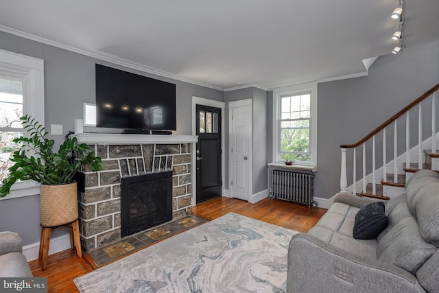 living room with radiator heating unit, wood finished floors, ornamental molding, a stone fireplace, and stairs