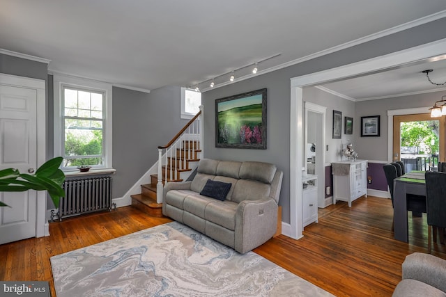 living area with radiator heating unit, track lighting, wood finished floors, stairs, and baseboards