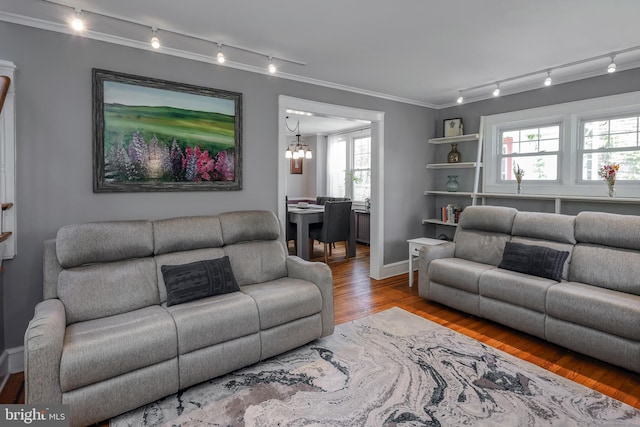 living room with track lighting, wood finished floors, a chandelier, ornamental molding, and baseboards