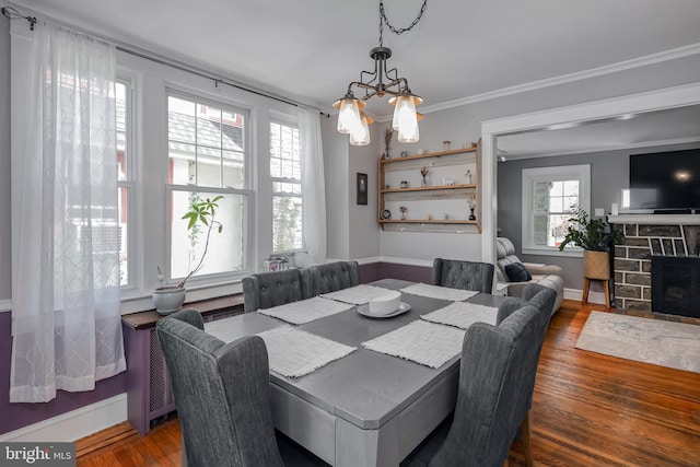 dining room featuring a chandelier, wood finished floors, baseboards, crown molding, and a stone fireplace