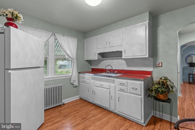 217 Lake Ave, Hamilton, NJ 08610 - kitchen with radiator, freestanding refrigerator, a sink, arched walkways, and light wood-style floors