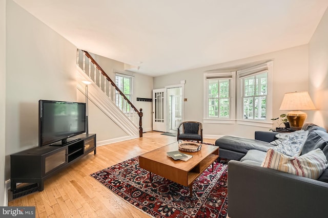 living area featuring stairs, light wood finished floors, and baseboards