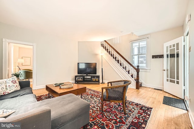 living room featuring stairs, light wood-type flooring, and baseboards