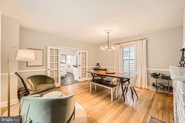 dining area featuring french doors, light wood-style flooring, a chandelier, and baseboards