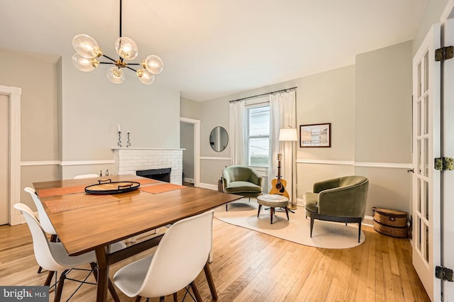 dining space featuring a fireplace, light wood-type flooring, a chandelier, and baseboards