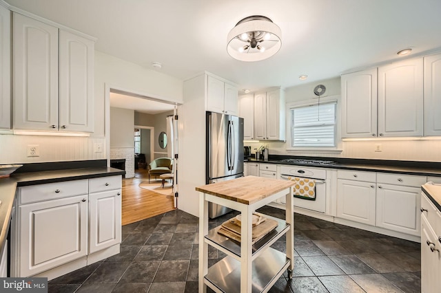 kitchen featuring freestanding refrigerator, white oven, dark countertops, gas cooktop, and white cabinets