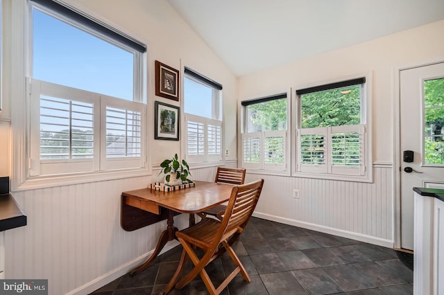 dining room with vaulted ceiling, a wainscoted wall, baseboards, and dark tile patterned flooring
