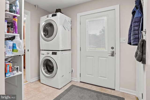 clothes washing area featuring estacked washer and dryer, light tile patterned flooring, and baseboards