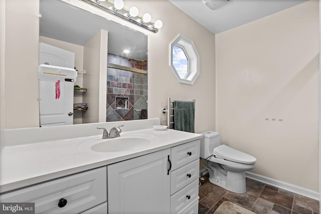 bathroom with stone tile floors, a tile shower, vanity, toilet, and baseboards
