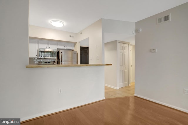 1001 N Randolph St Unit 109, Arlington, VA 22201 - kitchen with stainless steel appliances, white cabinets, light wood-style flooring, a peninsula, and backsplash
