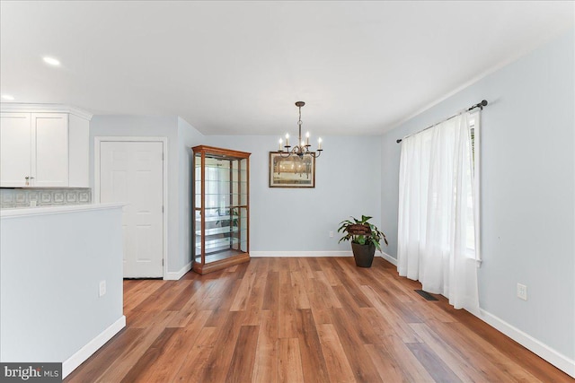 unfurnished dining area featuring a chandelier, light wood-type flooring, baseboards, and recessed lighting