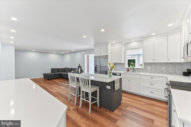 kitchen featuring appliances with stainless steel finishes, a sink, a kitchen island, white cabinets, and recessed lighting