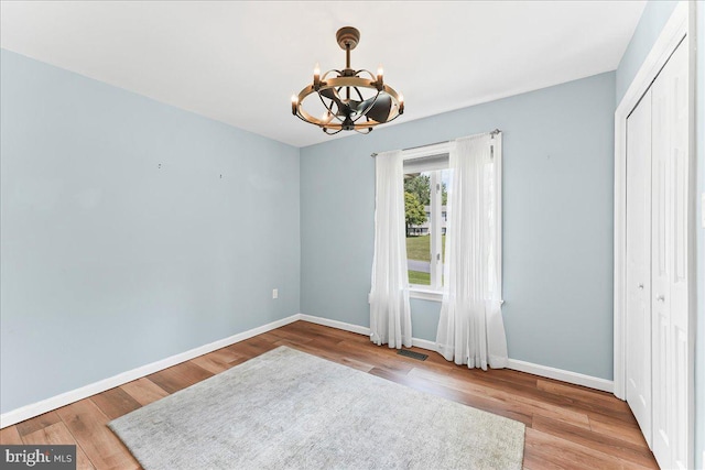 spare room featuring a chandelier, wood finished floors, and baseboards