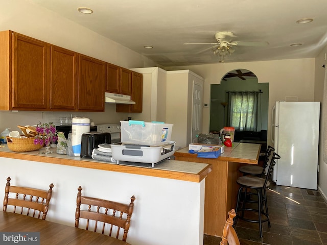 5110 Berclair Plantation Ln, Fredericksburg, VA 22408 - kitchen with freestanding refrigerator, a ceiling fan, a breakfast bar, under cabinet range hood, and brown cabinetry