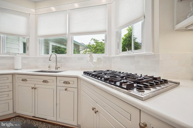 kitchen featuring a sink, stainless steel gas stovetop, tasteful backsplash, light countertops, and white cabinets