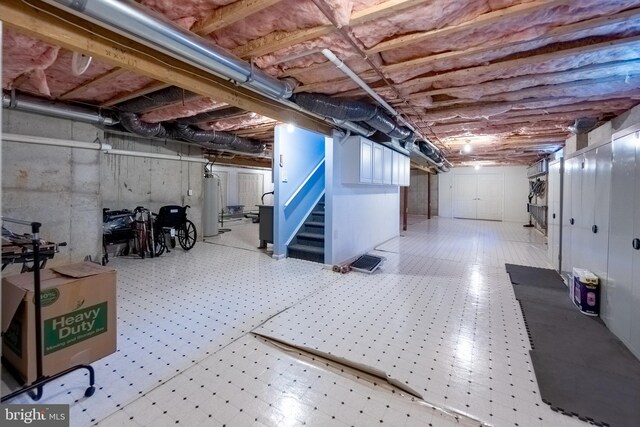 unfinished basement featuring tile patterned floors, gas water heater, and stairway