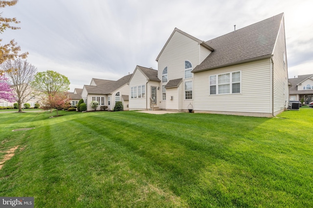 back of property featuring central air condition unit, a lawn, a patio, and roof with shingles