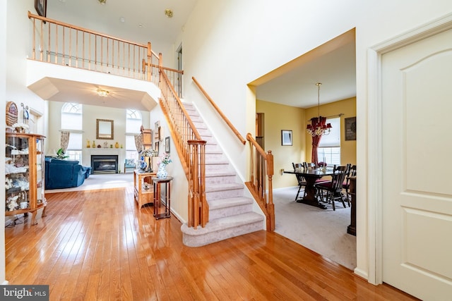stairs featuring a glass covered fireplace, a chandelier, hardwood / wood-style floors, a towering ceiling, and baseboards
