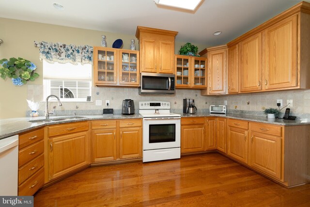kitchen featuring white appliances, a sink, tasteful backsplash, wood finished floors, and light stone countertops