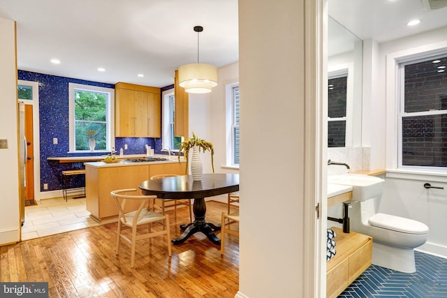 kitchen with light wood-style flooring, a peninsula, baseboards, backsplash, and decorative light fixtures