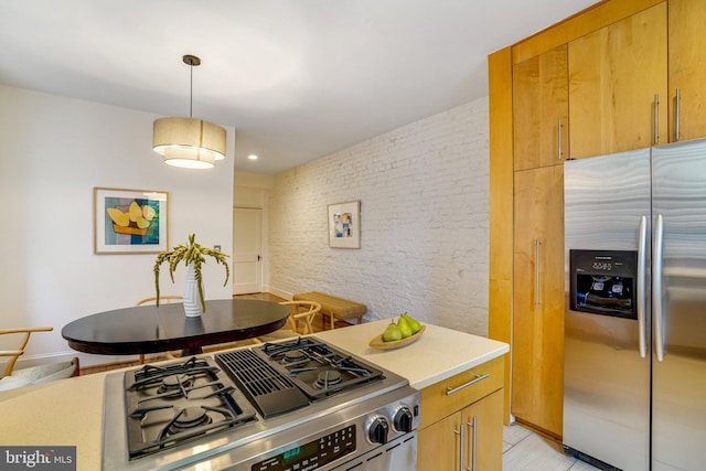 kitchen featuring appliances with stainless steel finishes, light countertops, brick wall, and hanging light fixtures