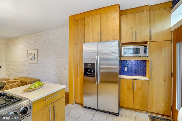 kitchen featuring stainless steel appliances, light countertops, and brick wall
