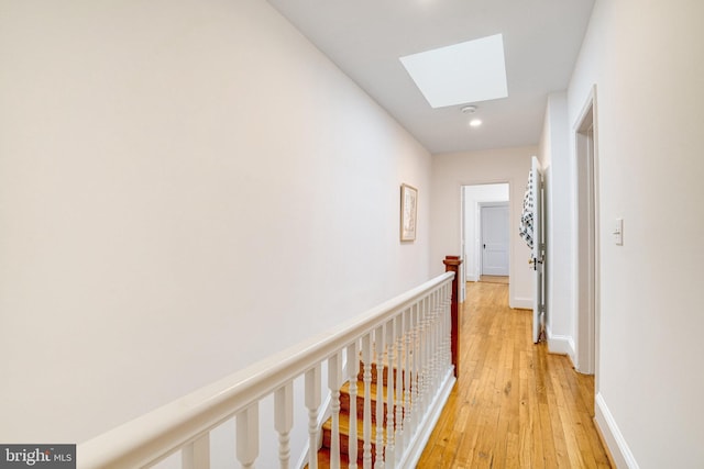 hallway with a skylight, light wood-style floors, an upstairs landing, baseboards, and recessed lighting